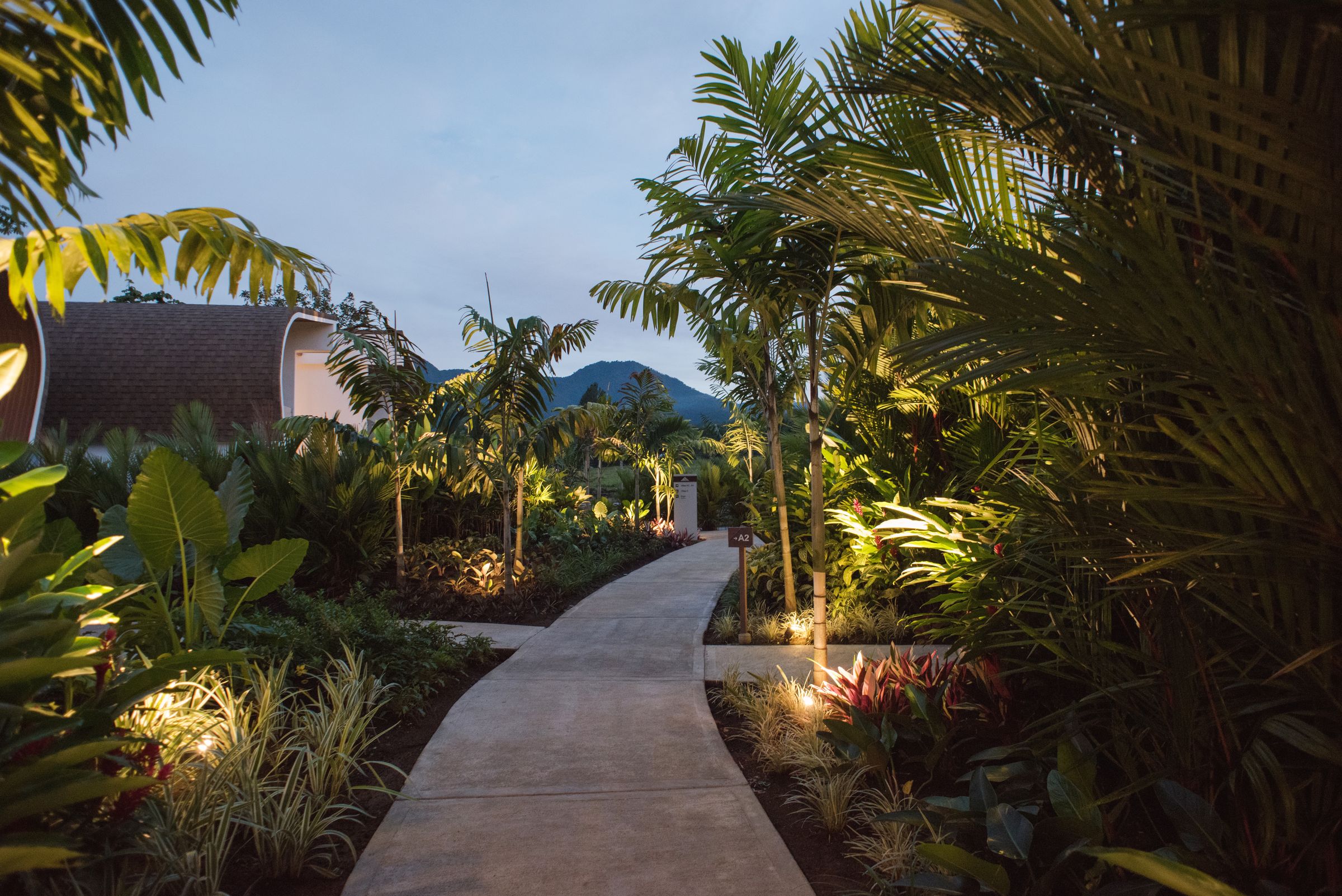 A lantern-lit garden path at dusk with Arenal Volcano in the distance